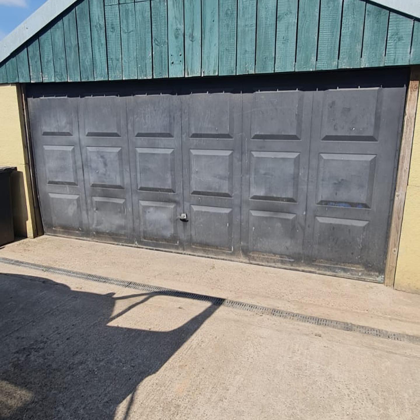Wide grey panelled garage door under a green timber gable
