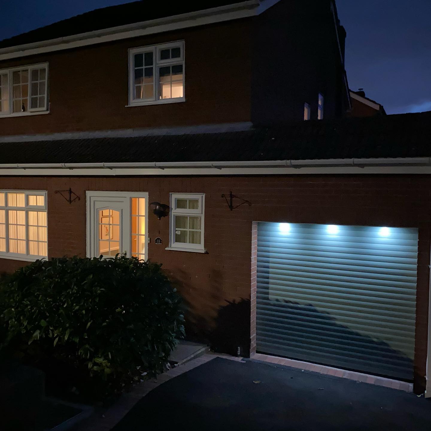 Brick home at dusk with a roller garage door lit by downlights